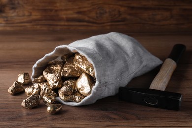 Photo of Overturned sack of gold nuggets and hammer on wooden table
