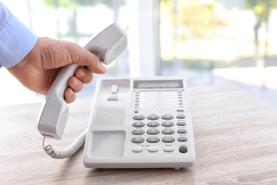 Photo of Man picking up telephone at table indoors