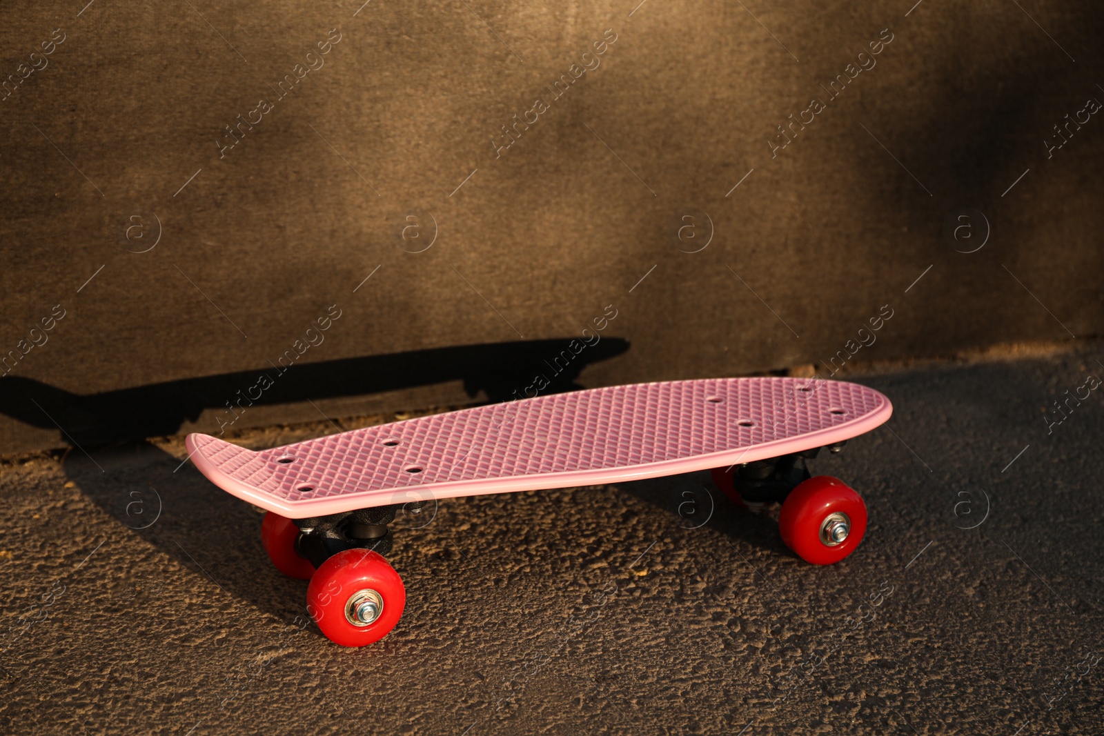 Photo of Modern pink skateboard with red wheels near black wall outdoors