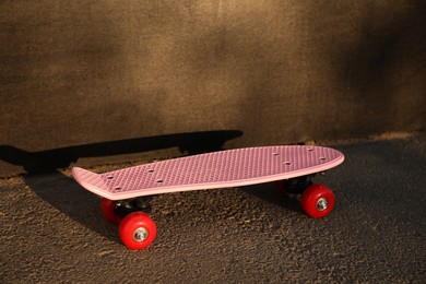 Modern pink skateboard with red wheels near black wall outdoors