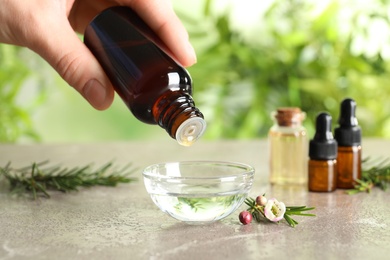 Photo of Woman dripping natural tea tree oil in bowl against blurred background, closeup