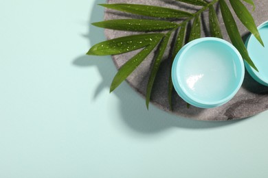 Photo of Lip balm and palm leaf on light blue background, top view. Space for text