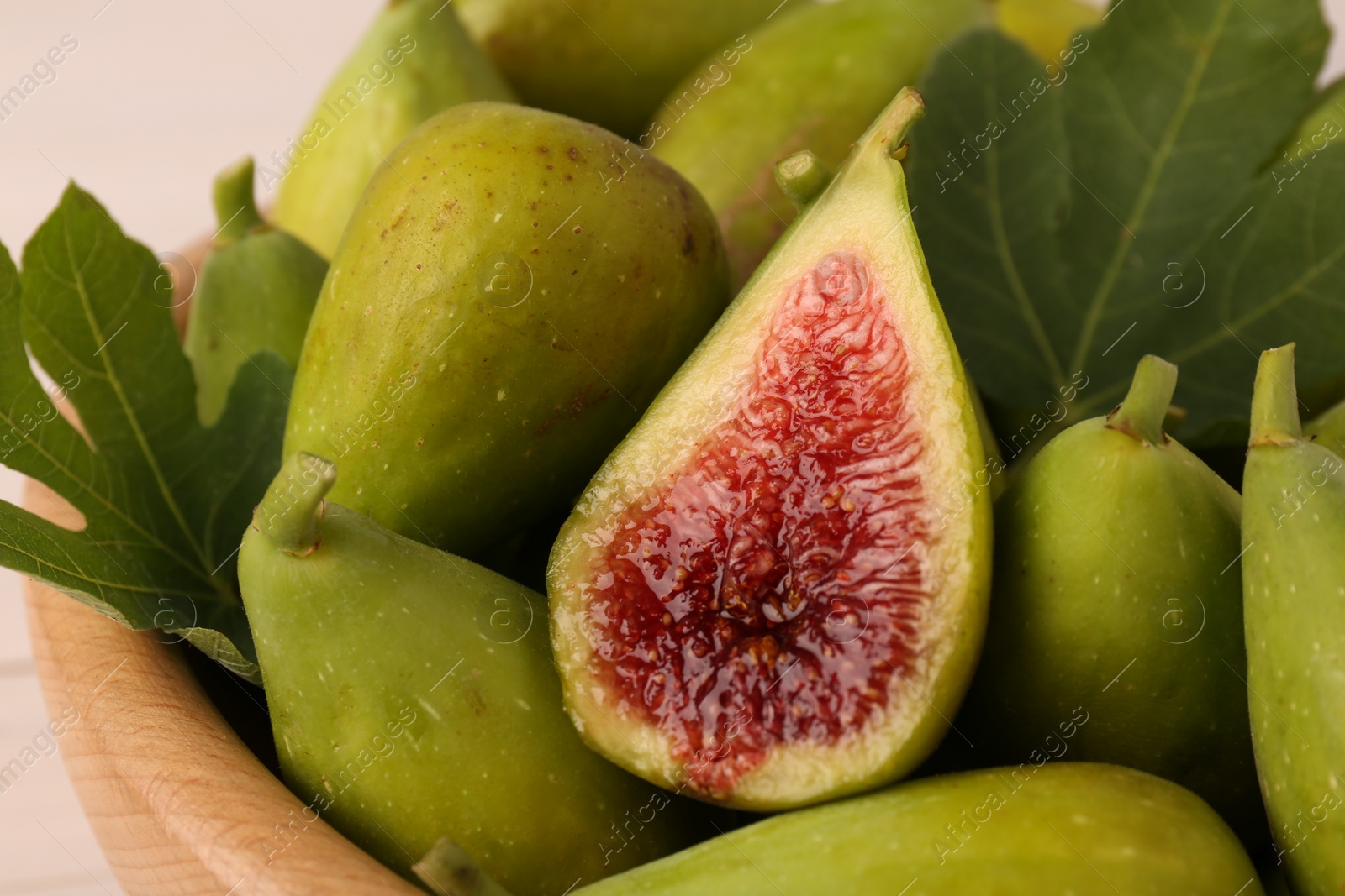 Photo of Cut and whole fresh green figs in wooden bowl, closeup
