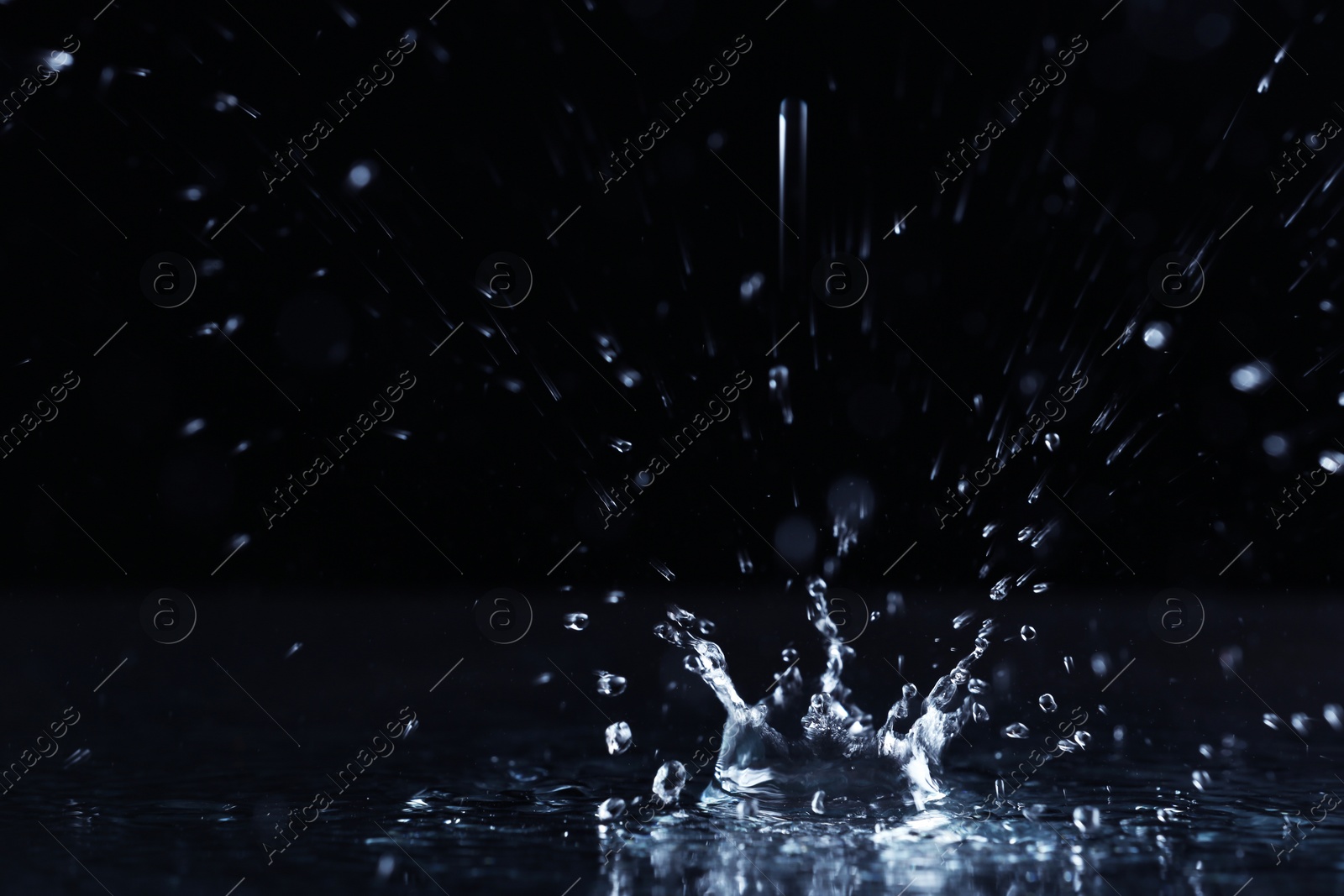 Photo of Rain drop falling down into puddle on dark background