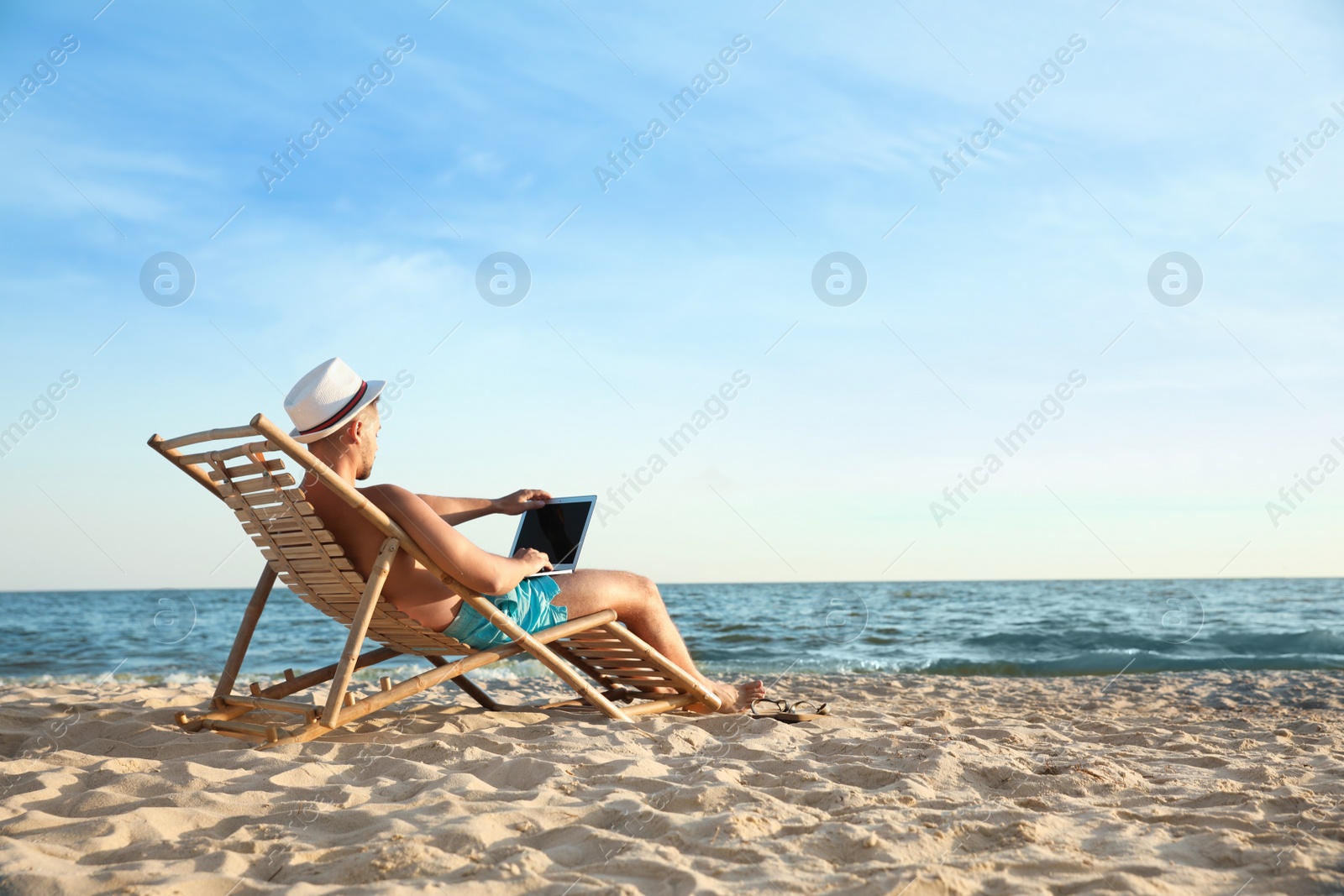 Photo of Young man with laptop in deck chair on beach