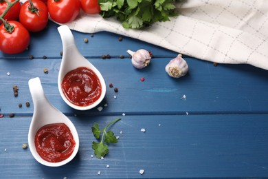 Photo of Organic ketchup in spoons, fresh tomatoes and spices on blue wooden table. Tomato sauce