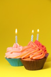 Delicious birthday cupcakes with bright cream on yellow background