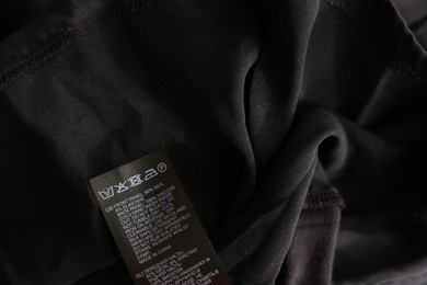 Photo of Clothing label in different languages on black garment, closeup