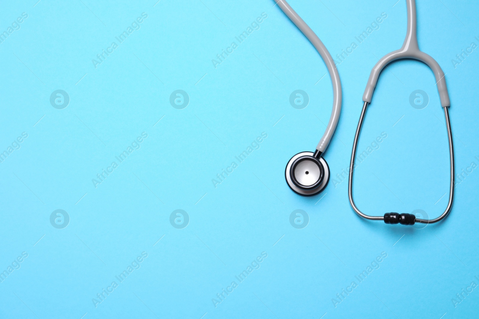 Photo of Stethoscope on light blue background, top view. Space for text