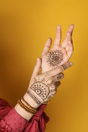 Photo of Woman with beautiful henna tattoos on hands against yellow background, closeup. Traditional mehndi