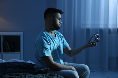 Photo of Tired man looking at alarm clock on bed