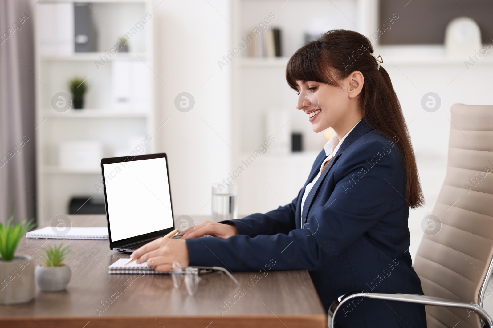 Photo of Woman taking notes during webinar at wooden table indoors