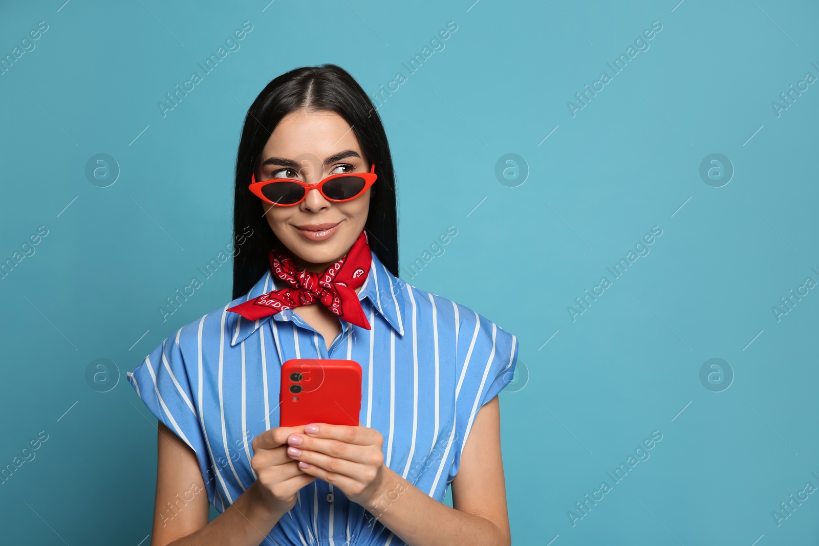 Photo of Fashionable young woman in stylish outfit with bandana using smartphone on light blue background, space for text