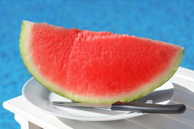 Photo of Slice of fresh juicy watermelon on white plate near swimming pool outdoors, closeup