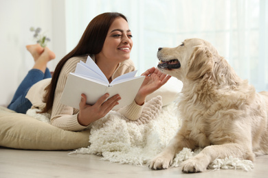 Photo of Young woman with book and her Golden Retriever at home. Adorable pet