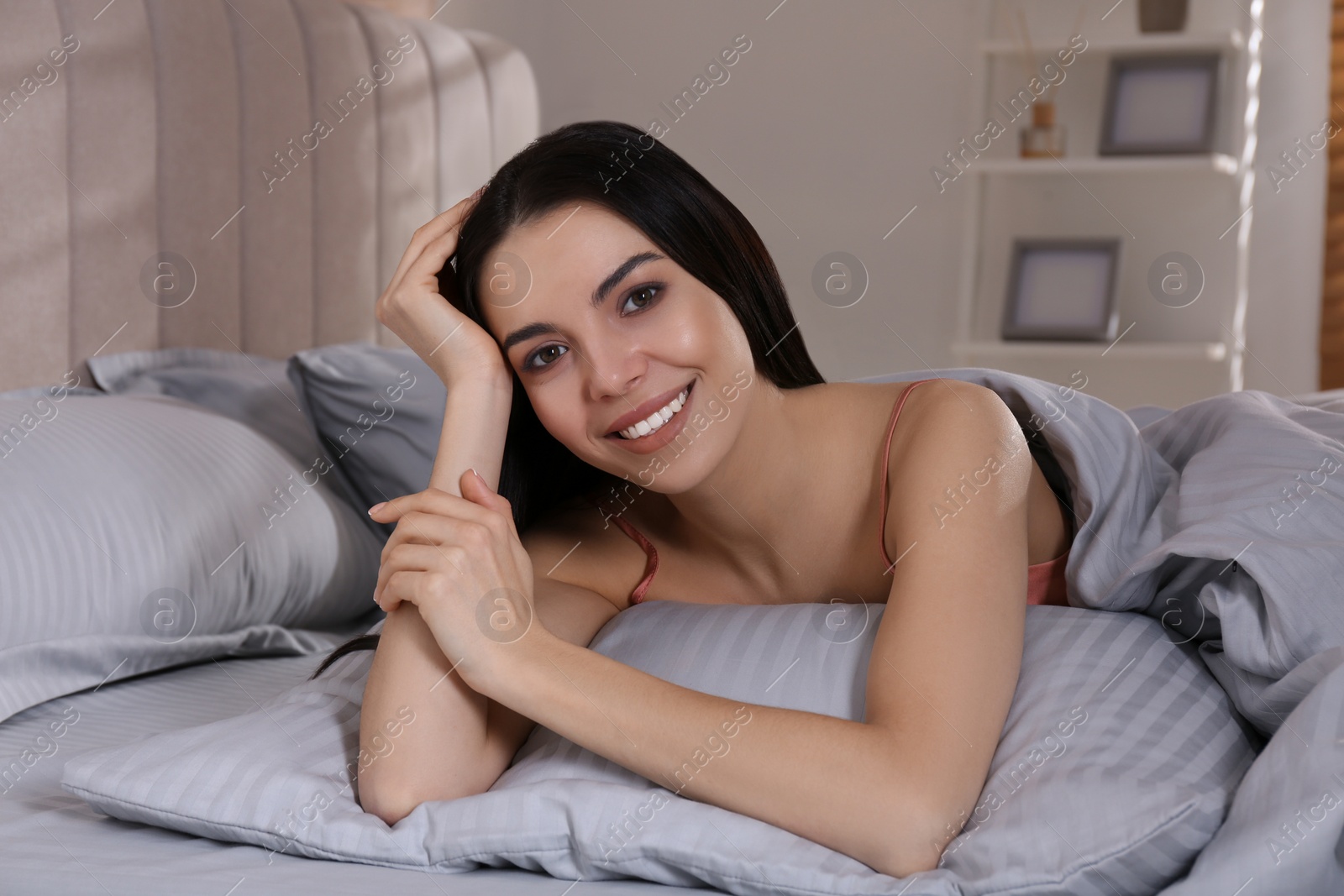 Photo of Woman lying in comfortable bed with light grey striped linens