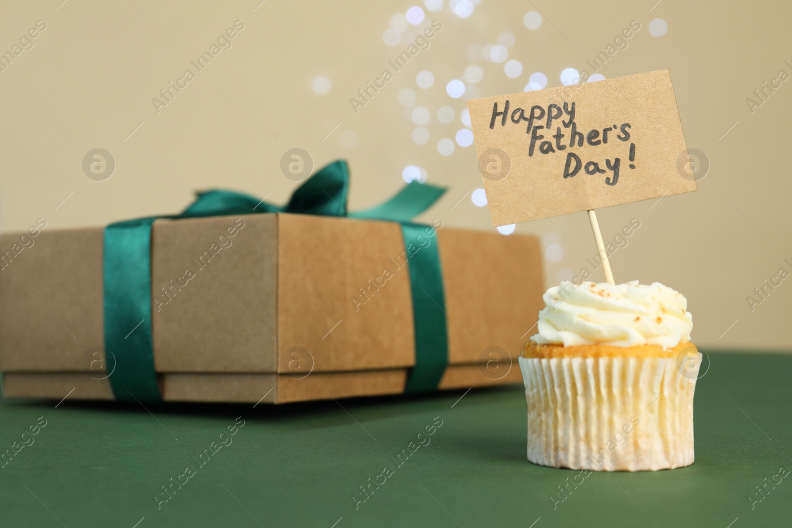 Photo of Happy Father's Day. Tasty cupcake with greetings and gift box on green table, closeup