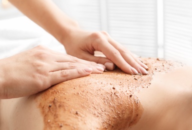 Photo of Young woman having body scrubbing procedure in spa salon, closeup