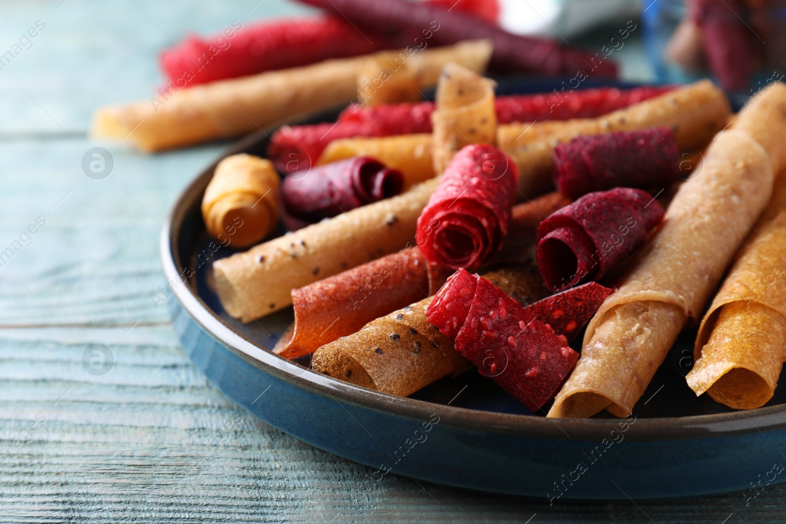 Photo of Delicious fruit leather rolls on blue wooden table, closeup