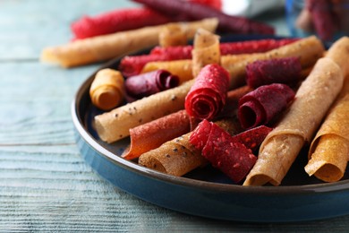 Photo of Delicious fruit leather rolls on blue wooden table, closeup