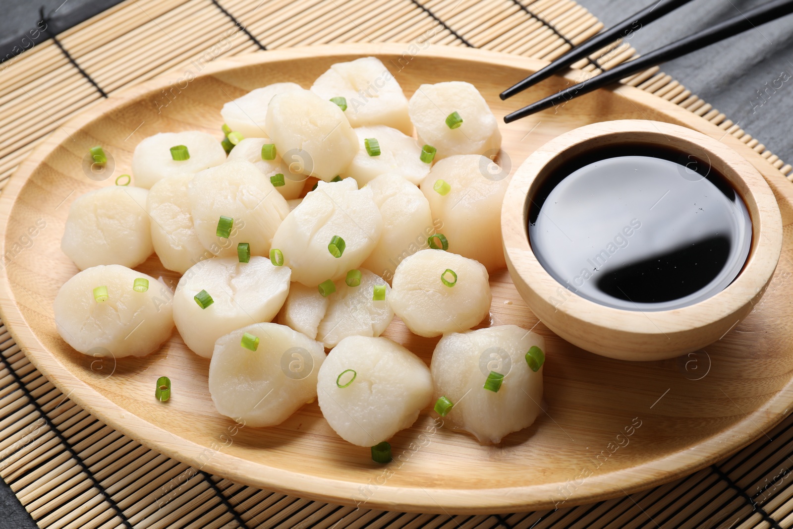 Photo of Raw scallops with green onion and soy sauce on dark table, closeup