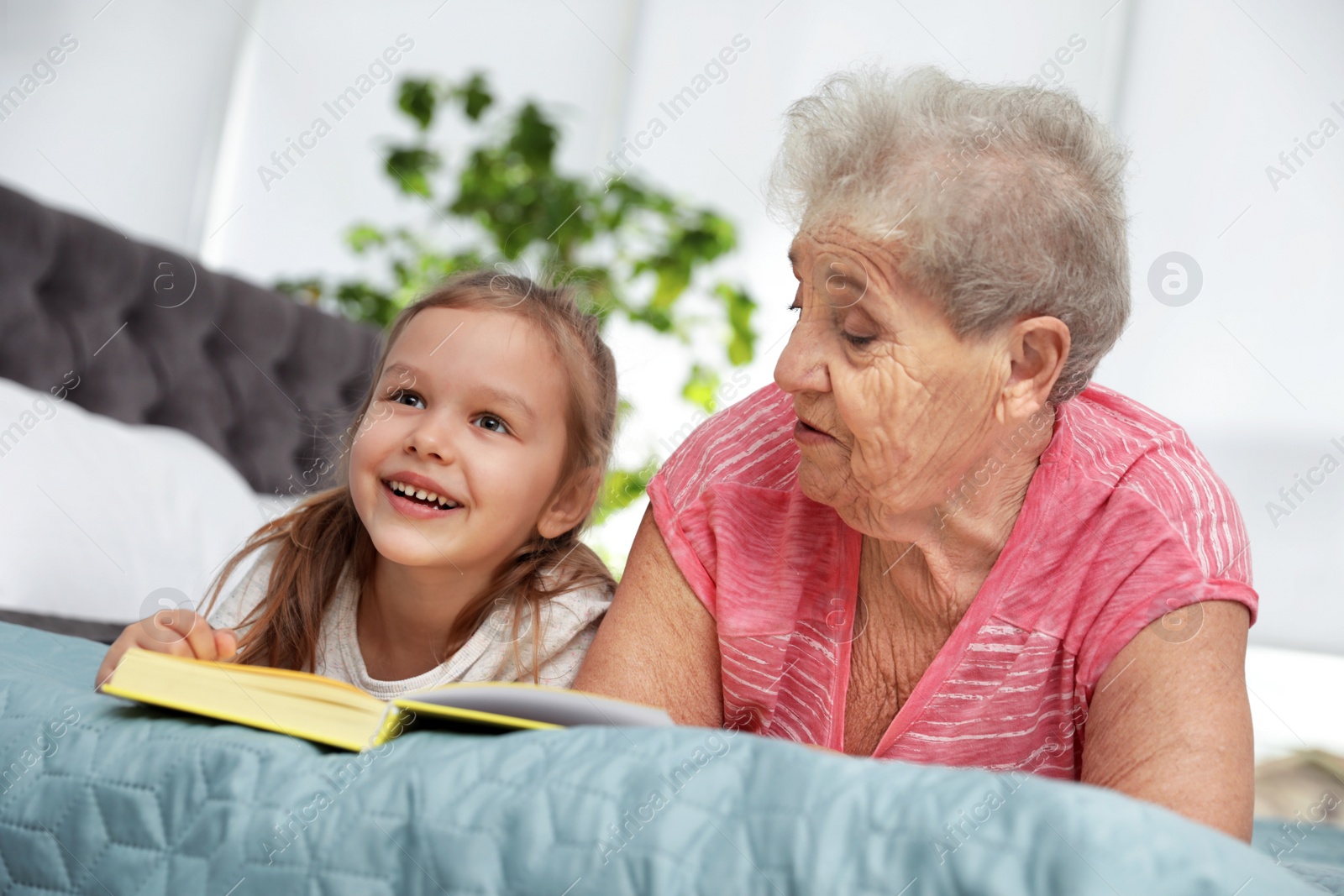 Photo of Cute girl and her grandmother reading book on bed at home