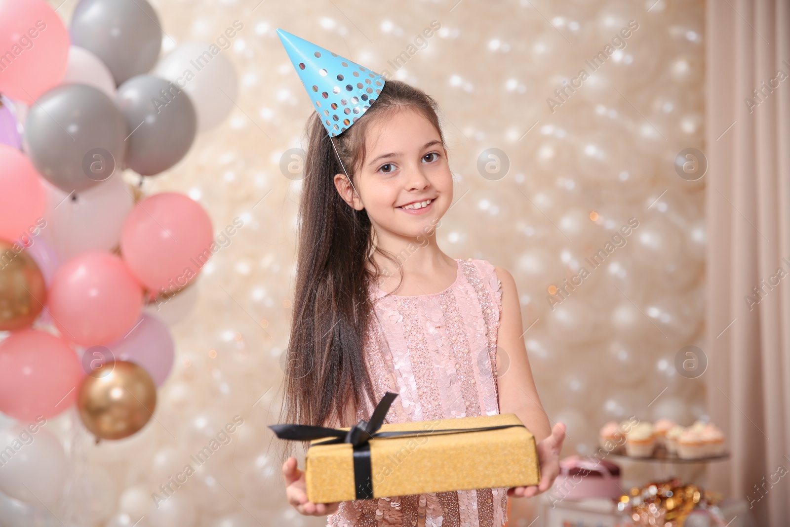 Photo of Happy little girl with gift in beautifully decorated room at home. Birthday celebration