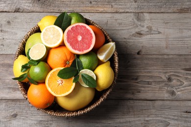 Photo of Different fresh citrus fruits and leaves in wicker basket on wooden table, top view. Space for text