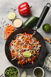 Photo of Shrimp stir fry with noodles and vegetables in wok surrounded by ingredients on grey table, flat lay