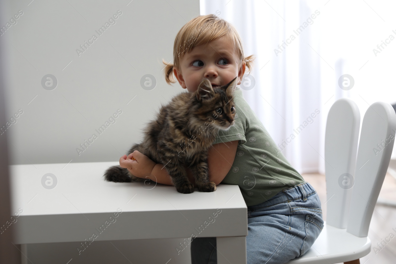 Photo of Cute little child with adorable pet at white table in room