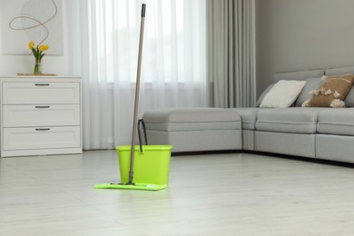 Photo of Mop and bucket on wooden floor in living room. Cleaning service