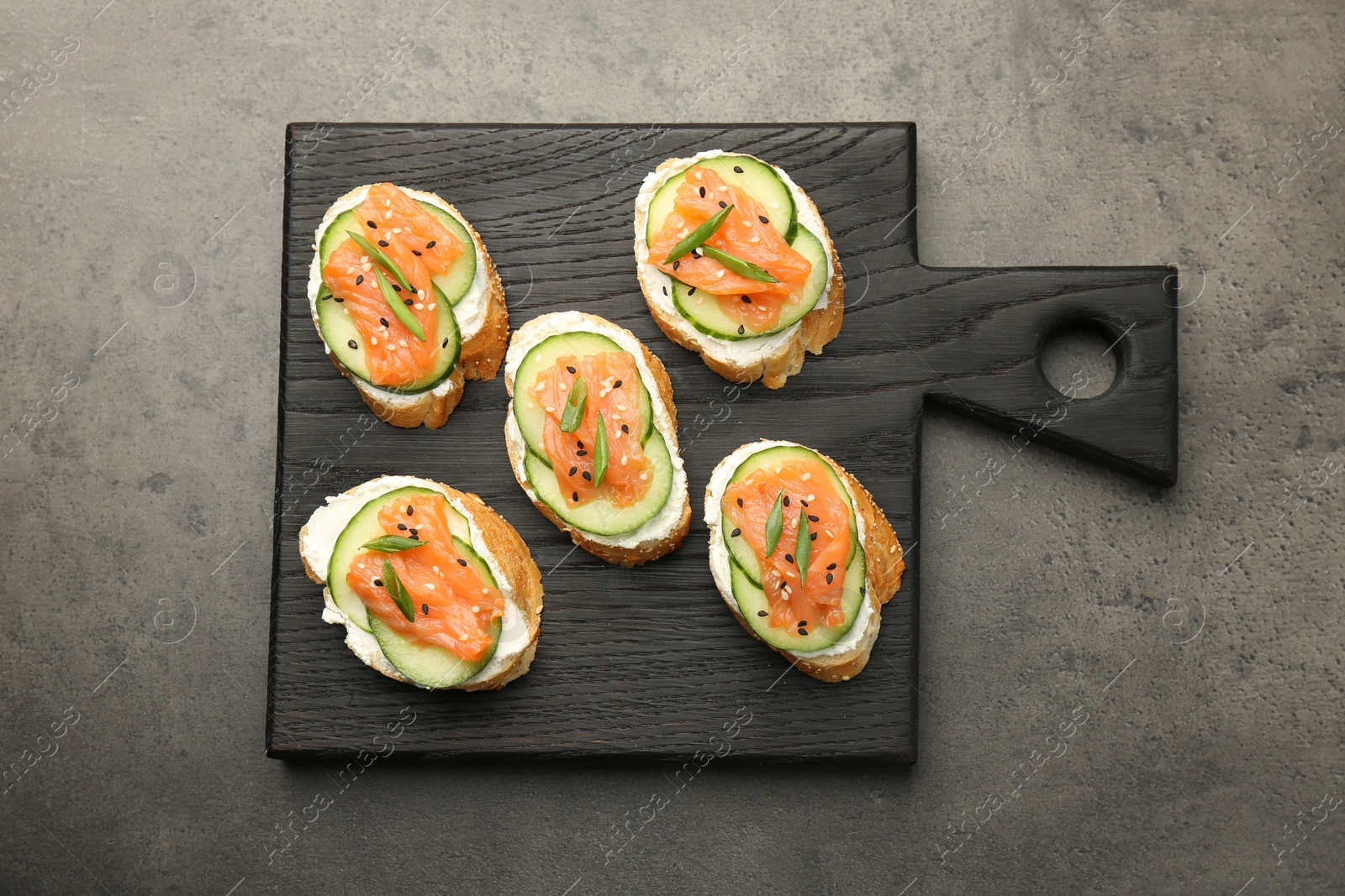 Photo of Tasty canapes with salmon, cucumber and cream cheese on grey table, top view