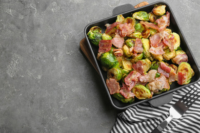 Photo of Delicious Brussels sprouts with bacon served on grey table, top view. Space for text