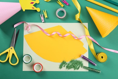 Photo of Handmade party hats, template and tools on green background, flat lay