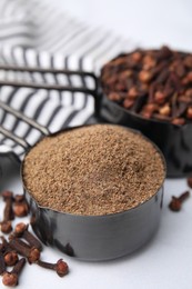 Aromatic clove powder and dried buds in scoops on white table, closeup