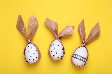 Photo of Easter bunnies made of craft paper and eggs on yellow background, flat lay