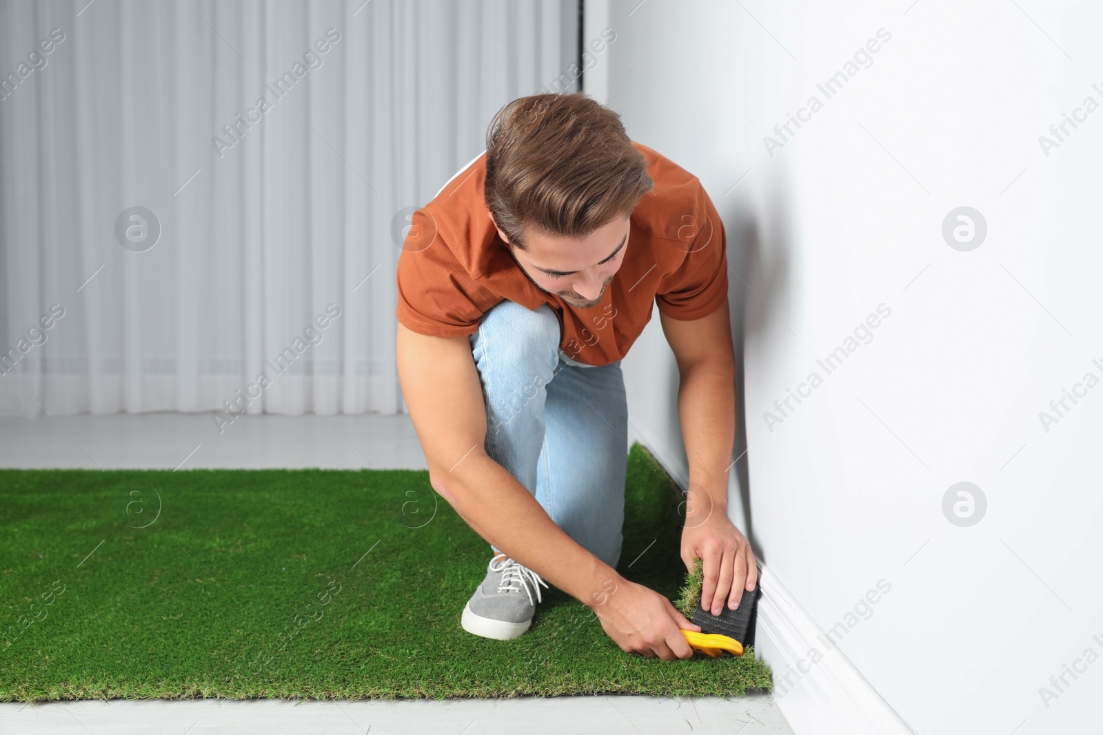 Photo of Man cutting artificial grass carpet indoors. Space for text