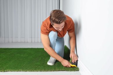 Photo of Man cutting artificial grass carpet indoors. Space for text