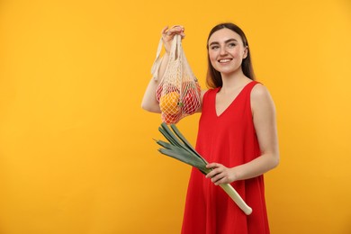 Photo of Woman with string bag of fresh vegetables on orange background, space for text