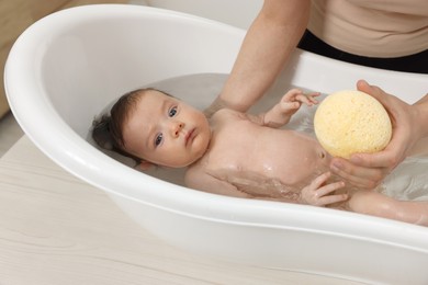 Mother bathing her little baby with sponge in bathtub, closeup