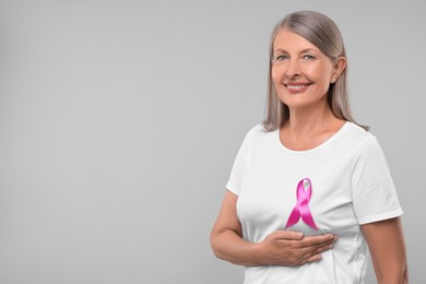 Photo of Beautiful senior woman with pink ribbon on light grey background, space for text. Breast cancer awareness