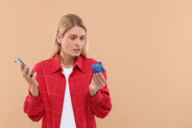 Photo of Stressed woman with credit card and smartphone on beige background, space for text. Be careful - fraud
