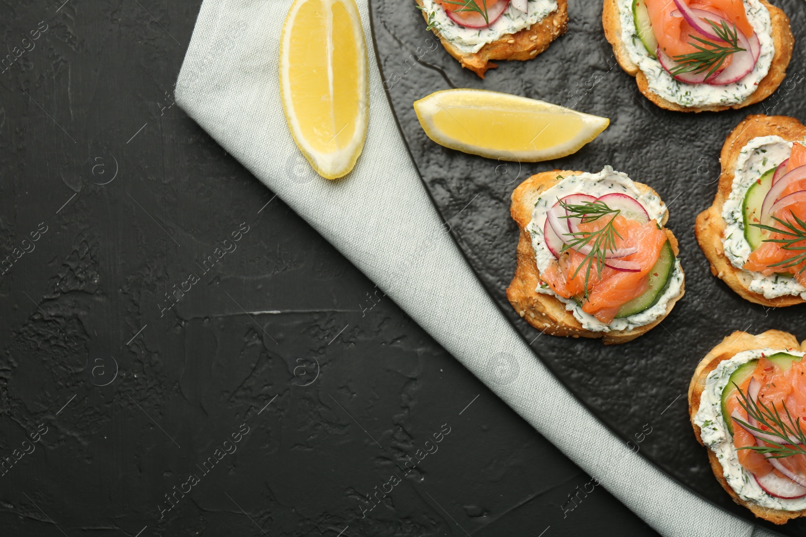 Photo of Tasty canapes with salmon, cucumber, radish and cream cheese on black table, top view. Space for text