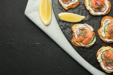 Tasty canapes with salmon, cucumber, radish and cream cheese on black table, top view. Space for text