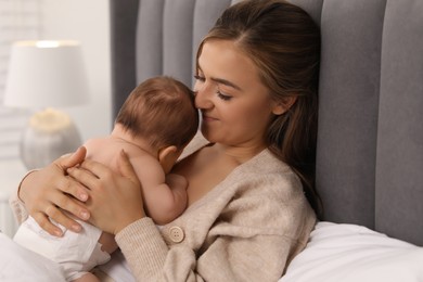 Mother holding her cute newborn baby on bed indoors