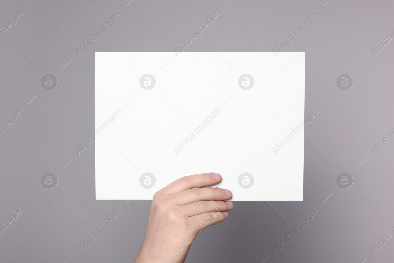 Photo of Woman holding sheet of paper on grey background, closeup. Mockup for design