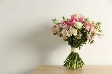 Photo of Beautiful bouquet of fresh flowers on wooden table near light wall. Space for text