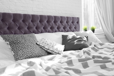 Photo of Bed with pillows and plaid near brick wall. Interior design