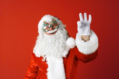 Photo of Authentic Santa Claus wearing funny glasses on color background