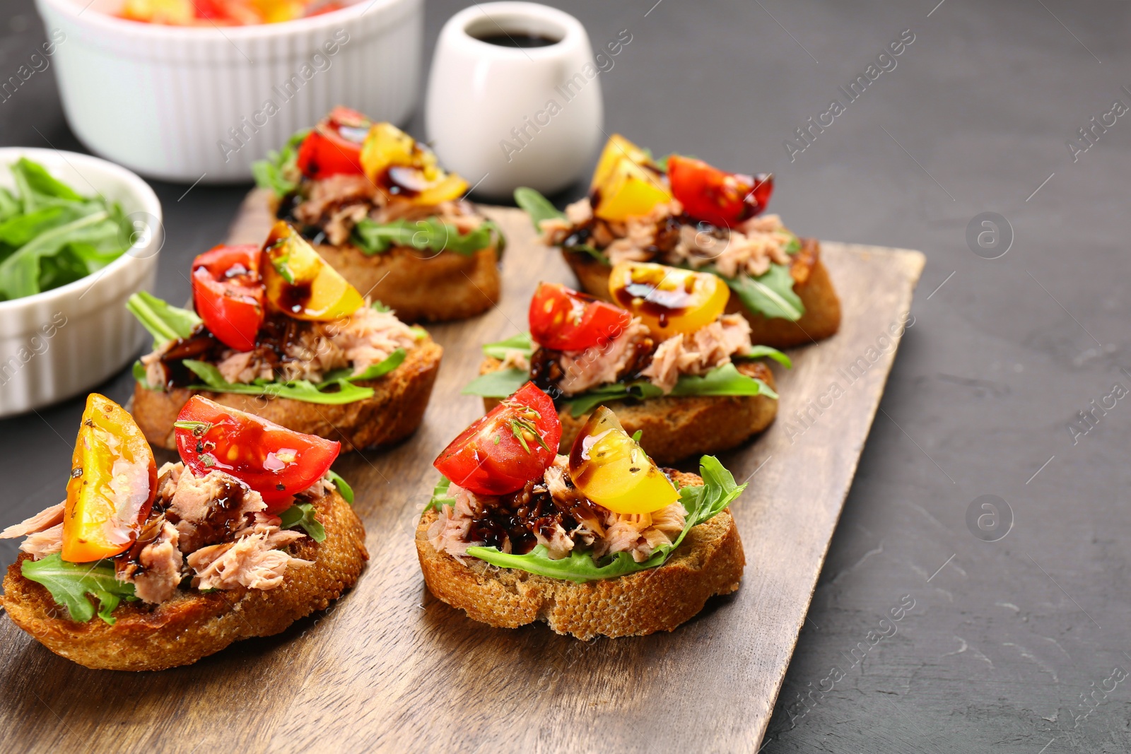 Photo of Delicious bruschettas with balsamic vinegar, tomatoes, arugula and tuna on grey textured table. Space for text